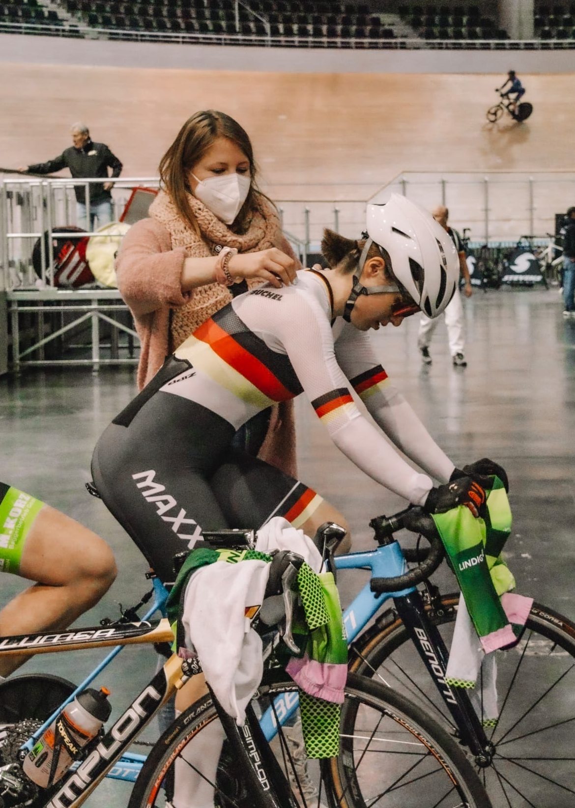 Auf der Radrennbahn, Sportlerin auf der Rolle in Deutschem Meister-Trikot, Betreuerin zupft an dem Einteiler herum